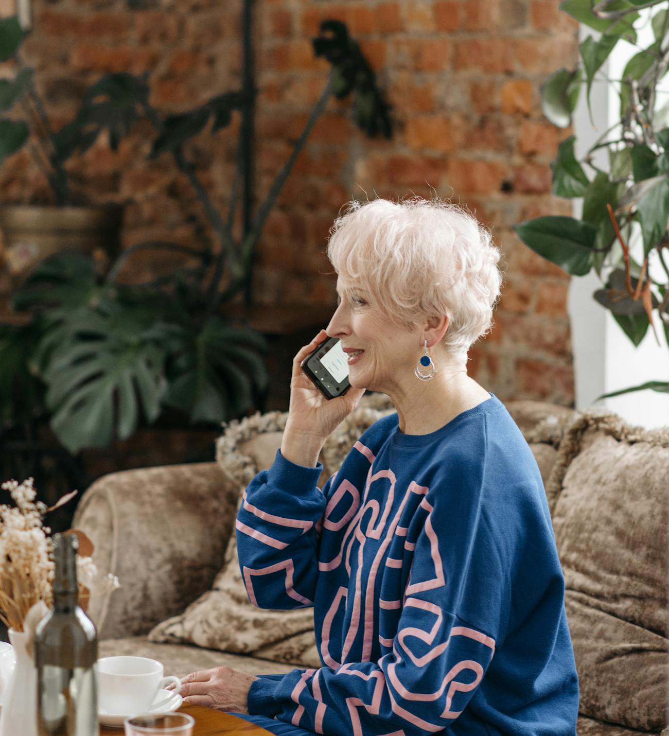 An older woman smiling warmly during a phone call by a sunlit window at home
